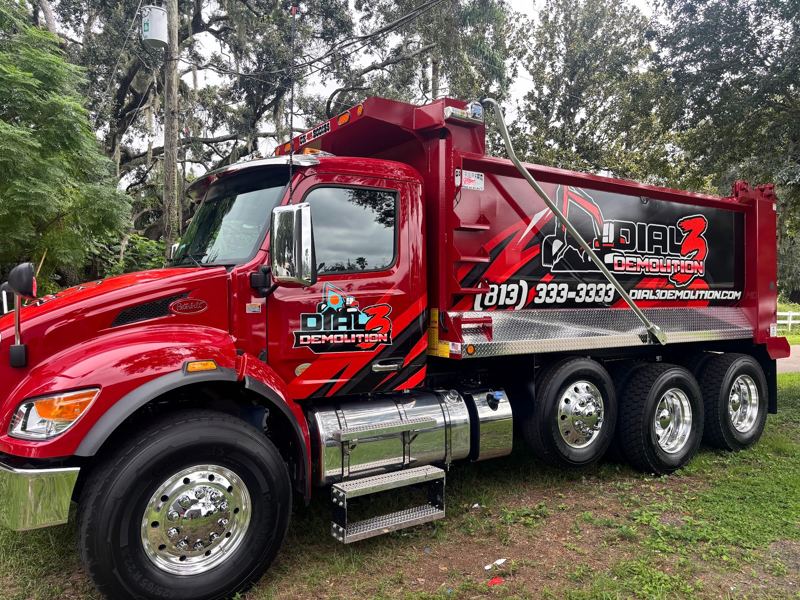 Red dump truck with company logo and phone number graphics